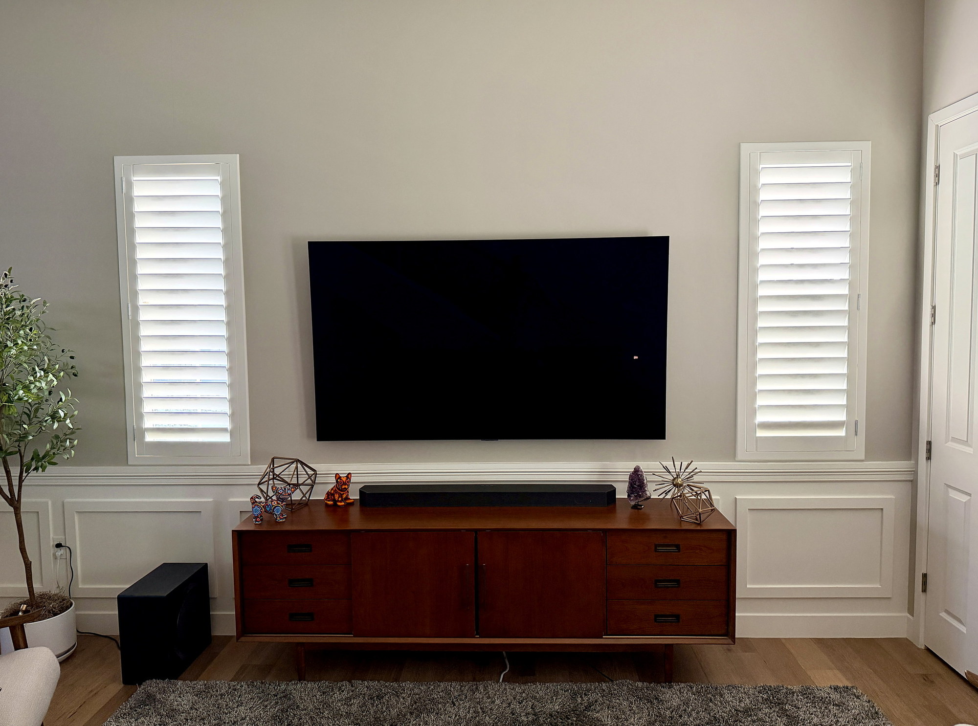 TV mounted above a mid-century walnut credenza between plantation shutters