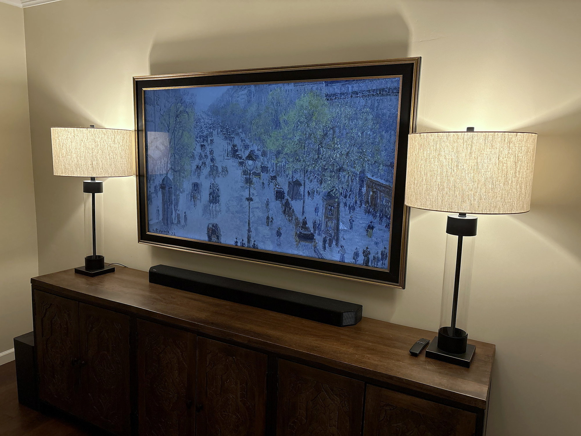 Frame TV in a gold bezel displaying a painting, flanked by table lamps