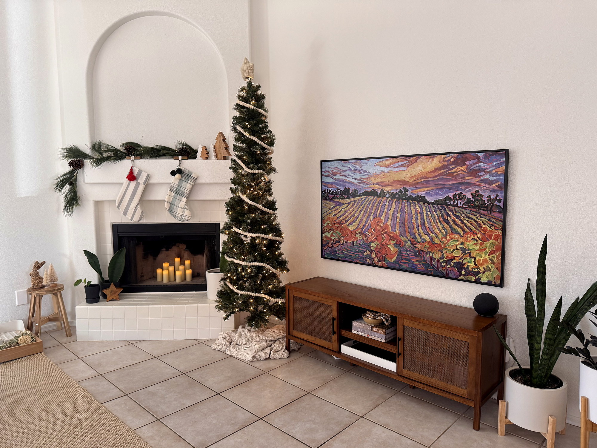 Frame TV displaying a landscape painting beside a decorated fireplace
