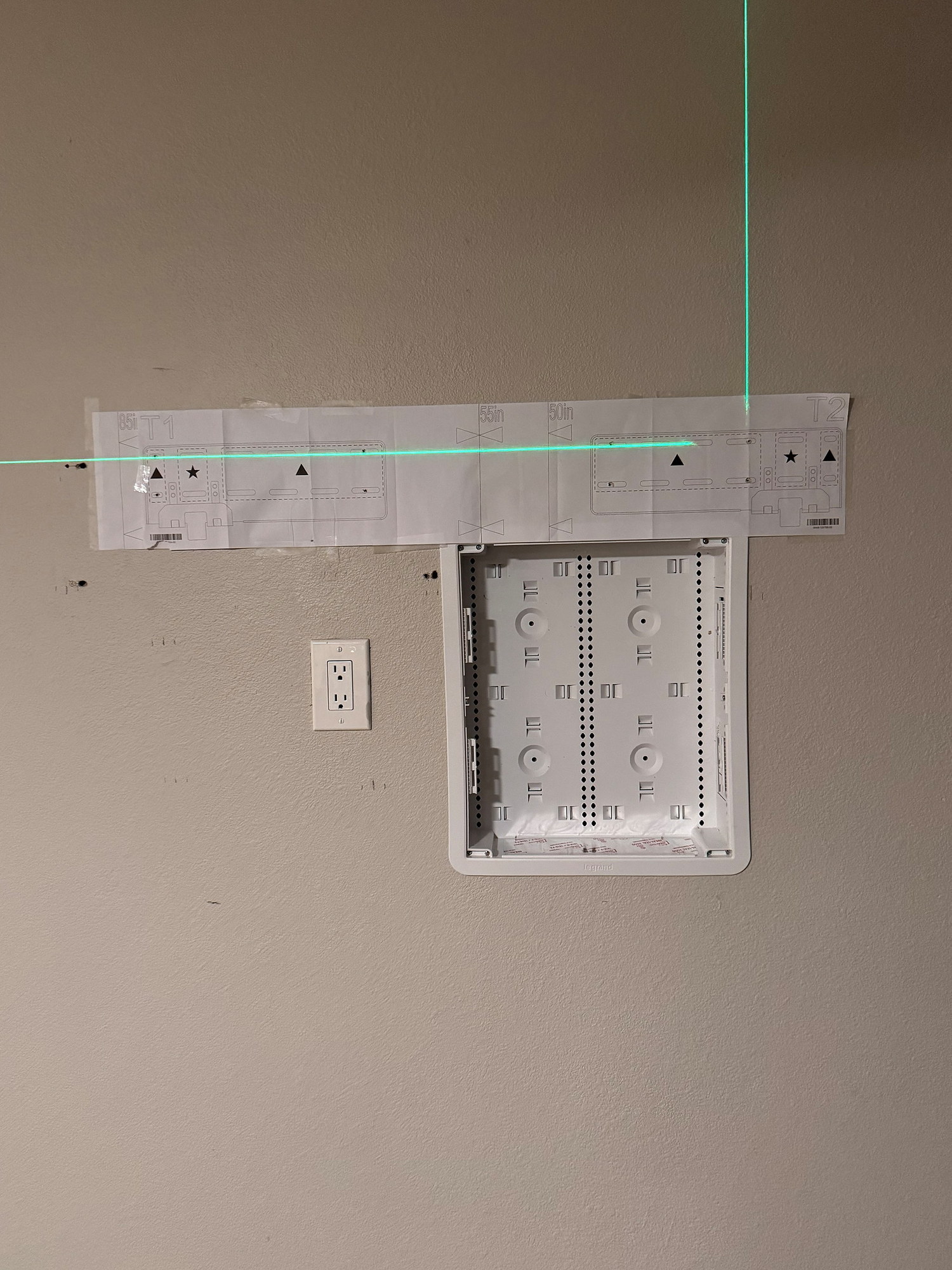 Green laser level line across a mount template and recessed wall box during layout